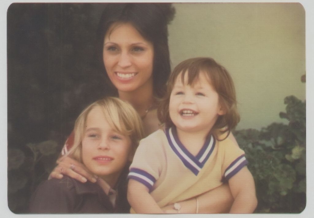 An archival photo of a mother with her two children. They are all smiling.