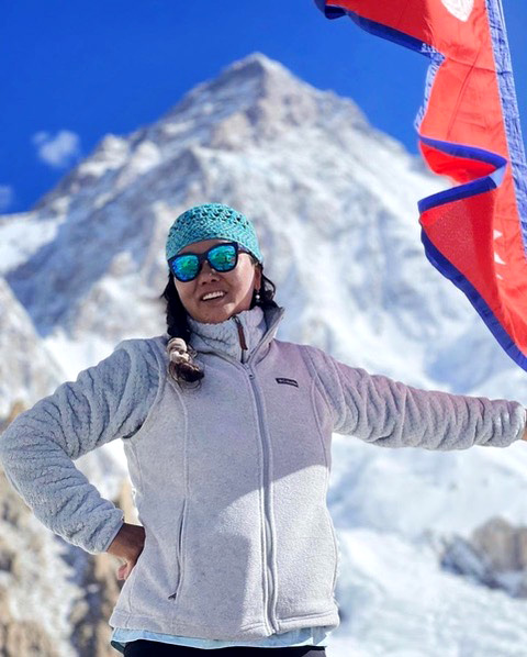 Lhakpa Sherpa poses with a red flag with blue trim at a base camp on Everest. The peak of the mountain is behind her.