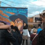 Two people hug amid a rally in the streets of Montreal. Behind them is a street art portrait of Nicholas Gibbs, a 23-year-old Black man.