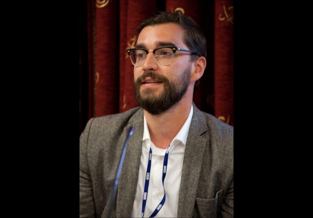 Gabor Pertic is a white man with brown hair and facial hair. He is pictured in close up at an industry event, wearing a grey blazer, white shirt, and glasses.