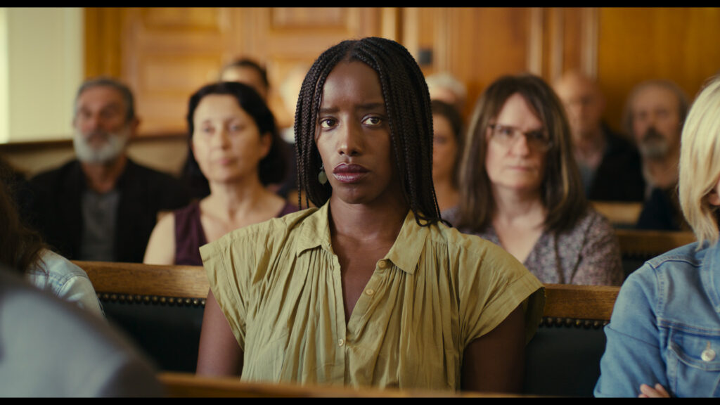 A woman stares off into the distance, sitting on a court bench surrounded by people