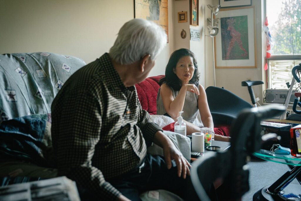 Director Min Sook Lee sits on a couch with her elderly father.
