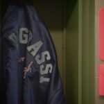 A school jacket hangs in a closet. It is blue with the letters DEGRASSI in white.