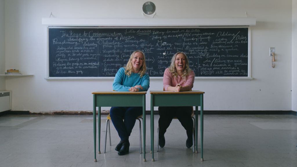 Twin sisters Angela Deiseach and Maureen Deiseach are seated in two desks in a high school classroom.