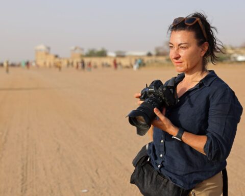 Photographer Lynsey Addario stands in a desert and holds a camera.