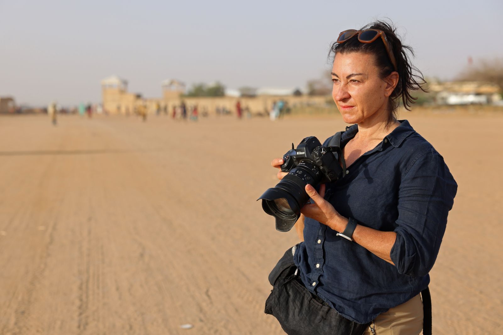 Photographer Lynsey Addario stands in a desert and holds a camera.