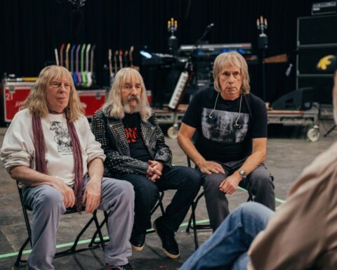 Three members of the rock band Spinal Tap, now in their 60s, sit on chairs in a recording studio