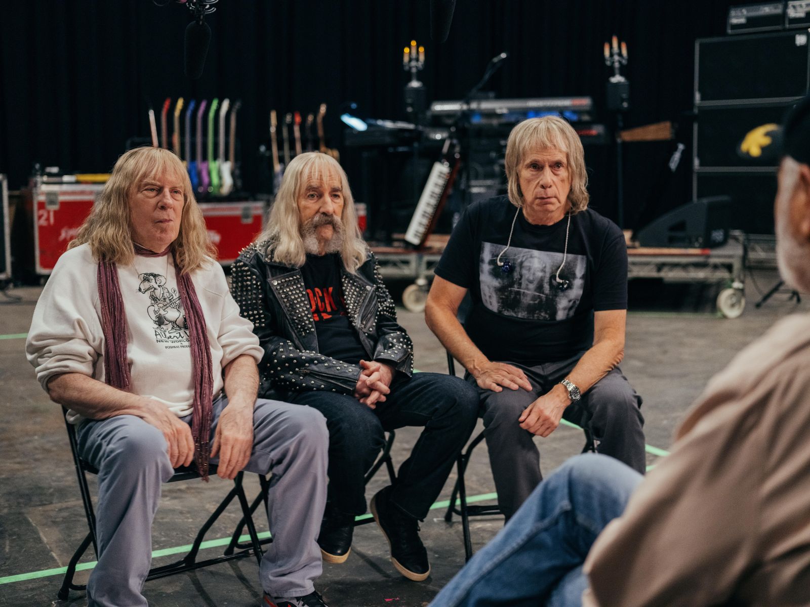 Three members of the rock band Spinal Tap, now in their 60s, sit on chairs in a recording studio