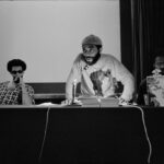 A black and white photo of a Black Power meeting from the 1960s with three Black men conducting a press conference.