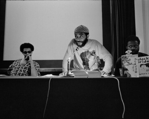 A black and white photo of a Black Power meeting from the 1960s with three Black men conducting a press conference.