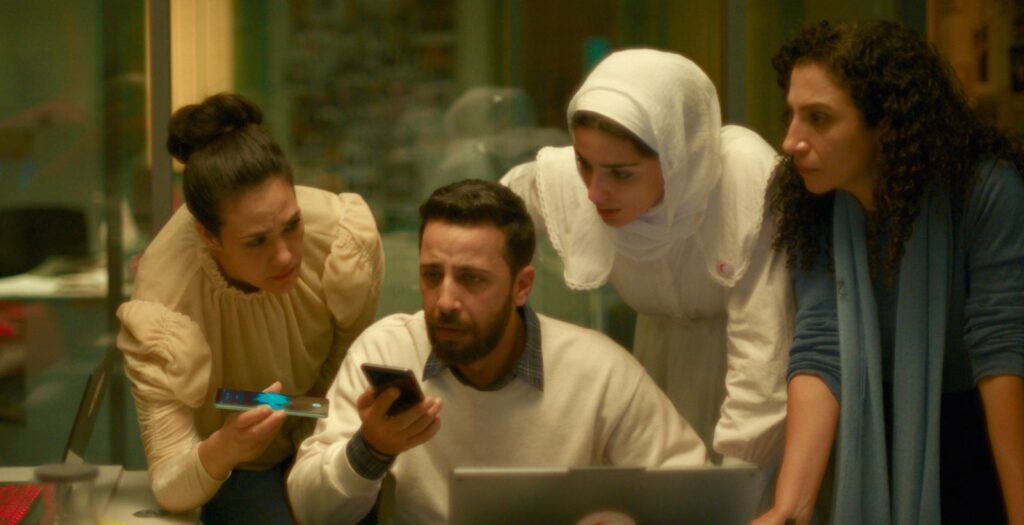A Palestinian man speaks on a cell phone on speaker mode as one man and two women lean over to hear.