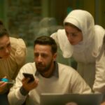 A Palestinian man speaks on a cell phone on speaker mode as one man and two women lean over to hear.