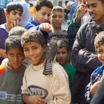 Children in Gaza pose for the camera and smile. The boy in the centre has a hawk on his shoulder.
