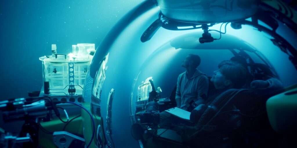 Two scientists--one woman and one man--are in an underwater research vessel. They both look up in awe.
