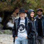 David Suzuki stands with Sarika Cullis-Suzuki and Anthony Morgan, the new generation of hosts for the Nature of Things. They are outside on a rainy day.