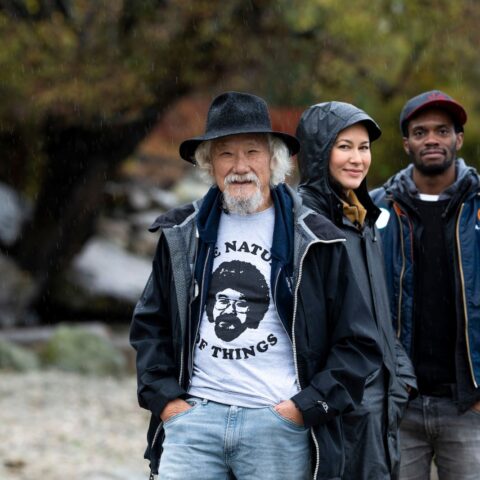 David Suzuki stands with Sarika Cullis-Suzuki and Anthony Morgan, the new generation of hosts for the Nature of Things. They are outside on a rainy day.