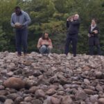 Four people stand in the distance atop of rocky shield in the forest.