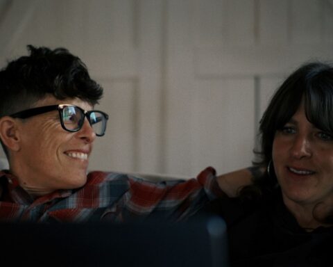 Poets Andrea Gibson and Megan Falley sit together on a couch in the documentary Come See Me in the Good Light. They are seen in a medium shot.