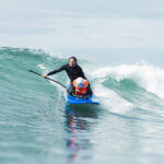An athlete crouches on a blue surfboard while riding a wave.