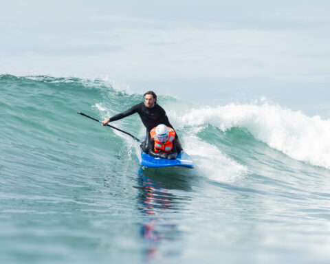 An athlete crouches on a blue surfboard while riding a wave.
