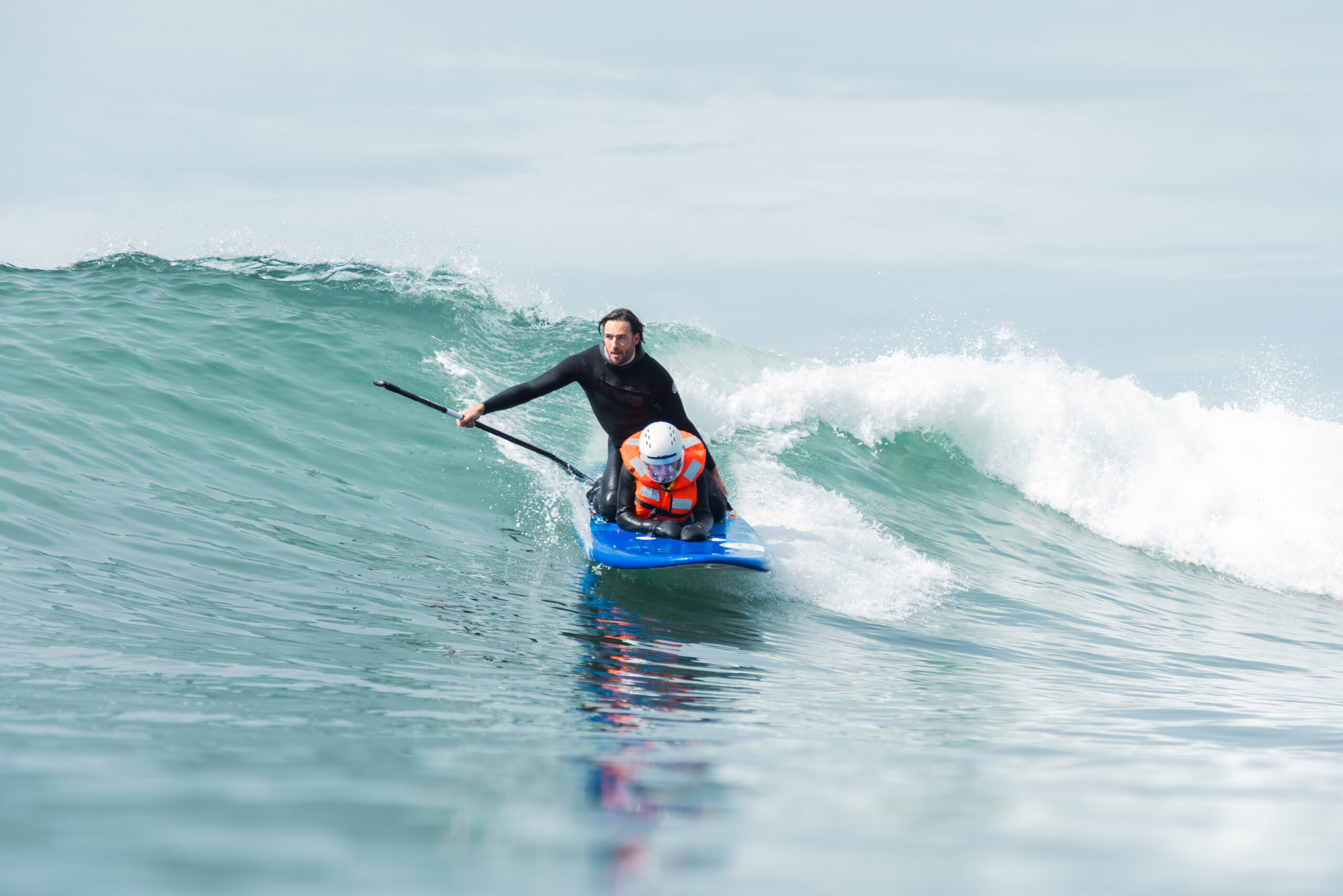 An athlete crouches on a blue surfboard while riding a wave.