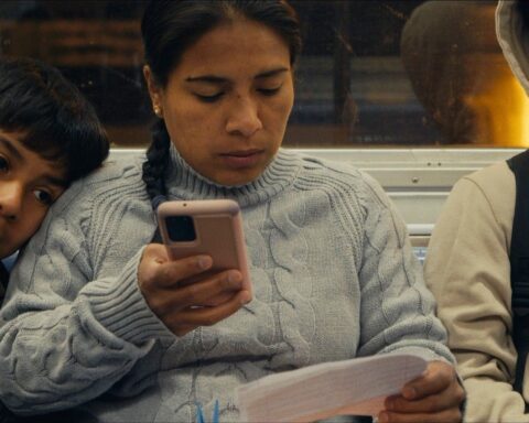 A Latin American woman rides the subway with her two sons. She is sitting between them reading a piece of paper and holding a phone.