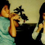 An old photograph of two young boys playing. They have their fists raised and are in a living room.