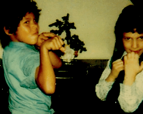 An old photograph of two young boys playing. They have their fists raised and are in a living room.