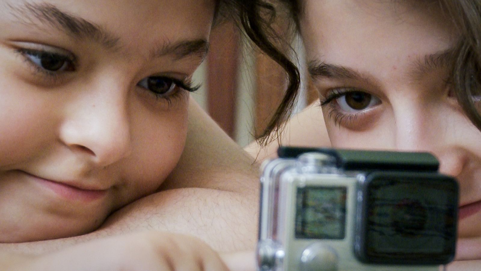 Two young Iranian girls sit closely together and look into the lens of a camera. They are pictured in closeup.