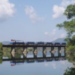 A train crosses a bridge that stretches over a river.