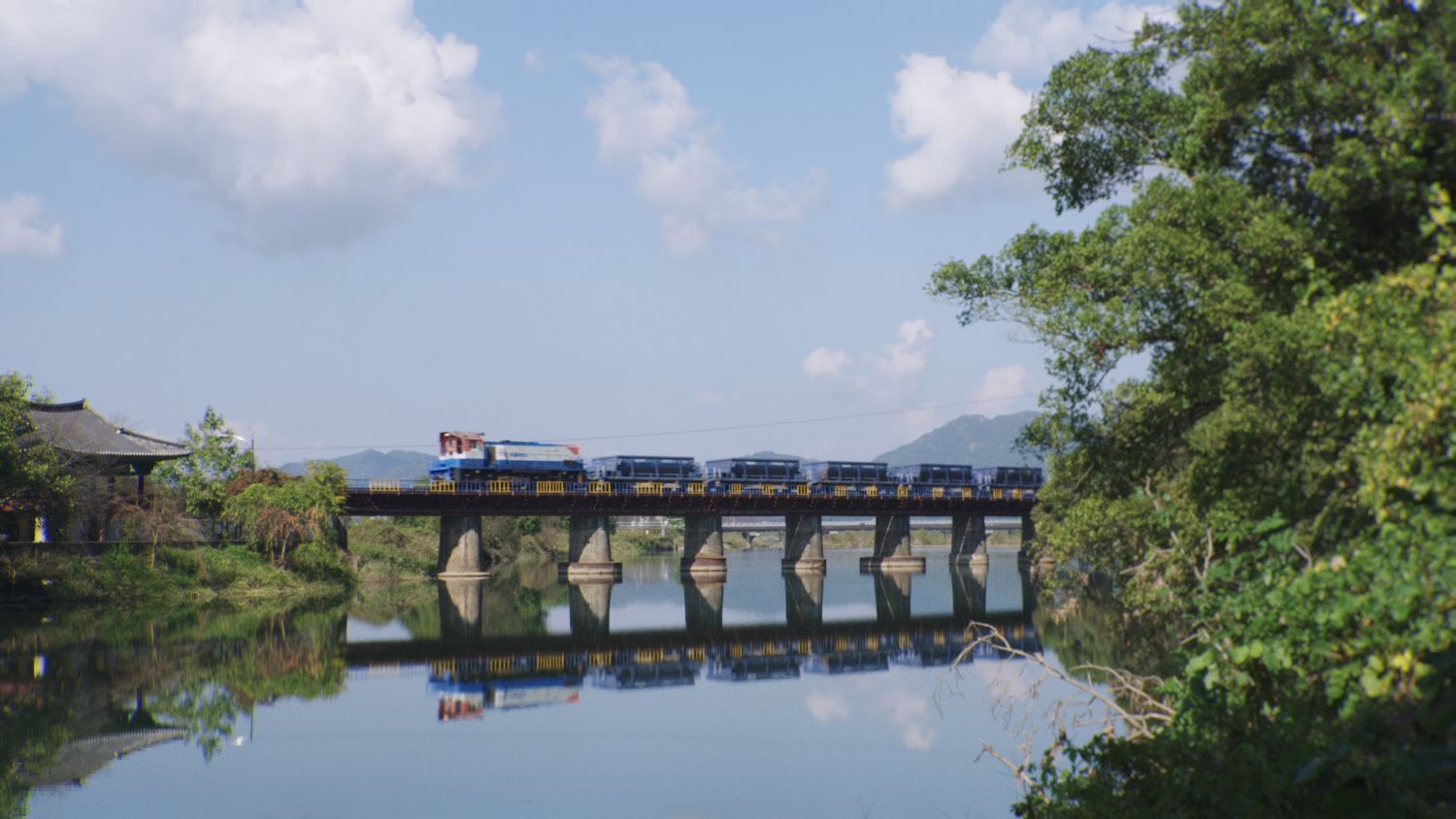 A train crosses a bridge that stretches over a river.