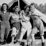 A black and white photo of four women standing in front of a tent.