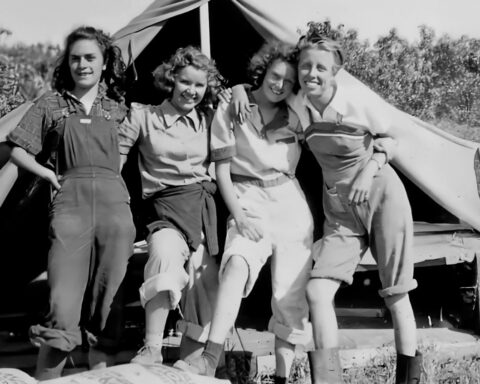 A black and white photo of four women standing in front of a tent.