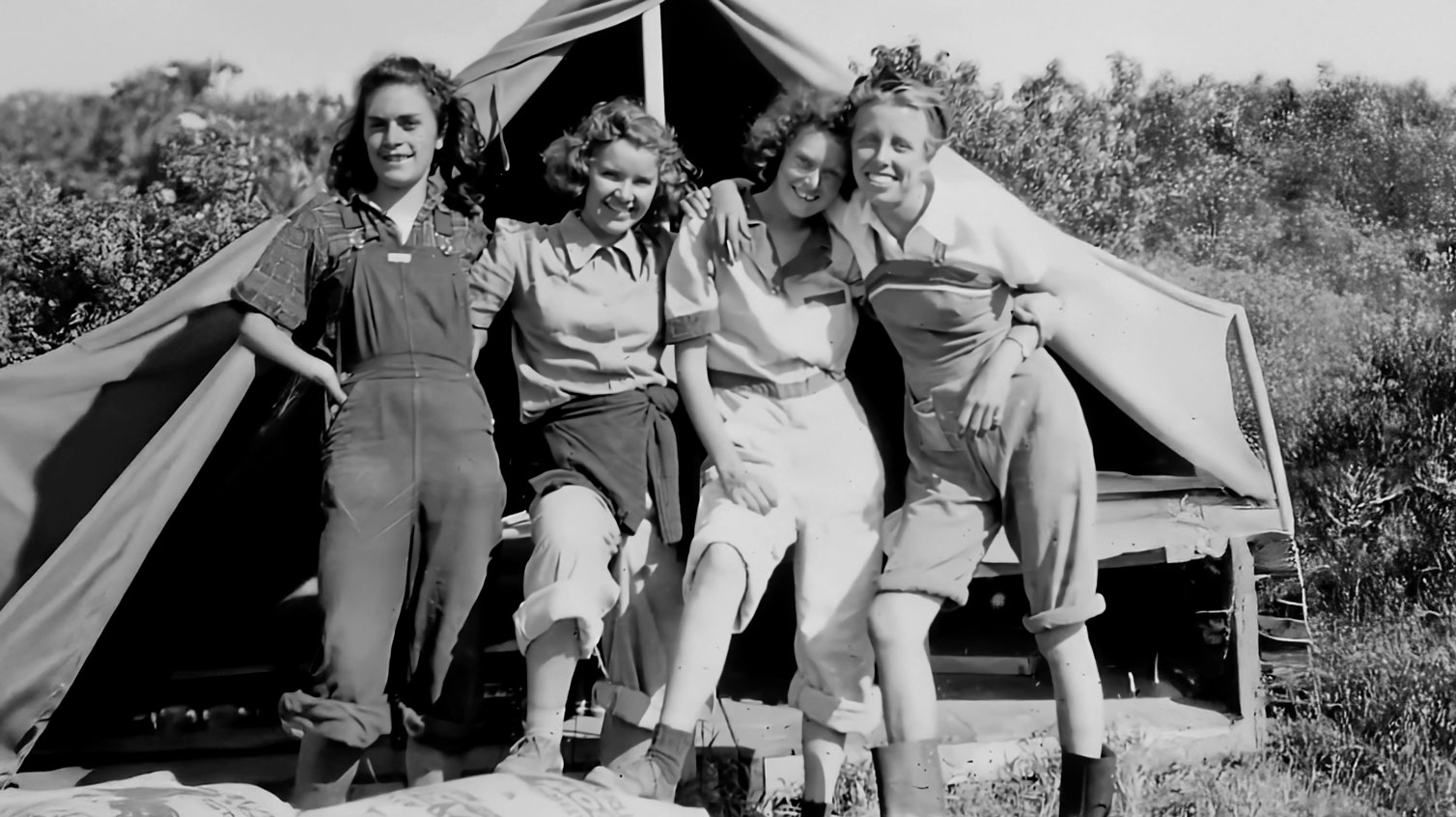 A black and white photo of four women standing in front of a tent.