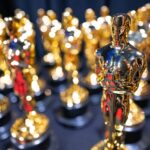 An Oscar statuette is seen in focus, standing in front of four rows of statuettes that are out of focus.