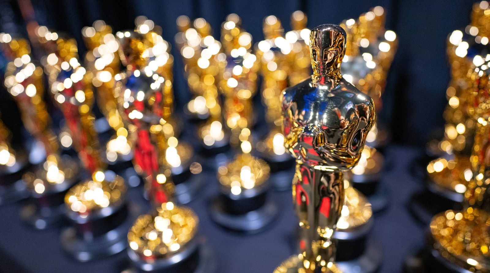 An Oscar statuette is seen in focus, standing in front of four rows of statuettes that are out of focus.