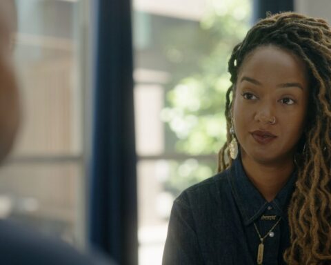 Amanda Parris is seated facing an off-screen interviewee. She is a Black woman with blond braided hair, and is wearing a dark blue collared shirt.