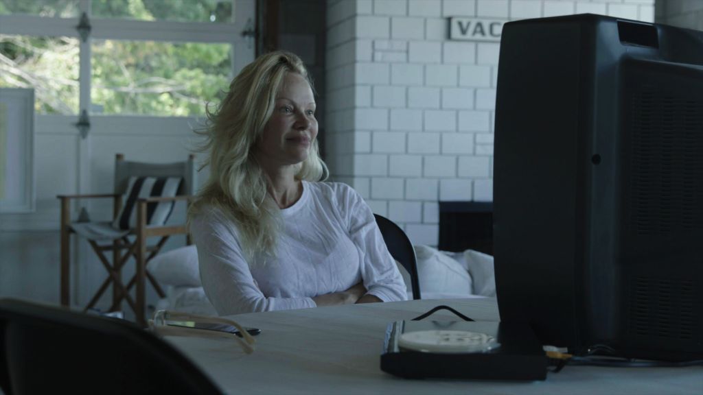 Actress Pamela Anderson sits at her kitchen table. She is a white woman with blond hair brushed to the side. She has no make-up on and is wearing a white shirt.