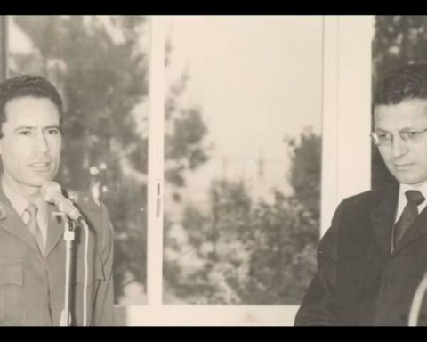 An archival black and white image of a young Muammar Gaddafi standing with a man in a suit.