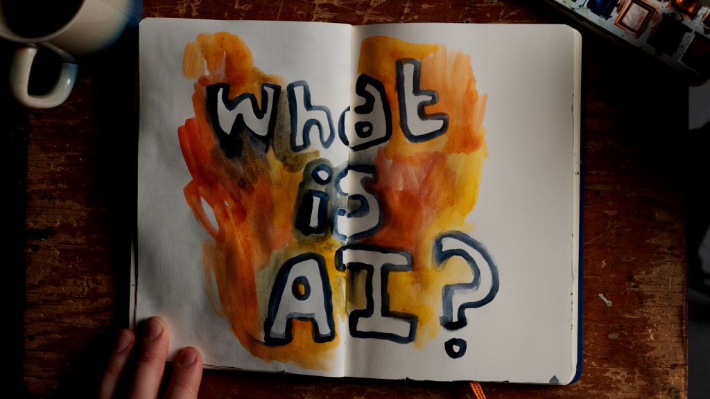 A notebook has the words "What Is AI?" written in bubble letters and surrounded by orange flames.