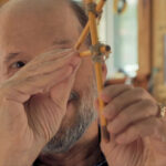 A man looks through a compass made with three pencils tied together with twine.