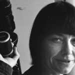 A black and white archival photo of a young Barbara Hammer. She is holding a camera and seen in close-up.