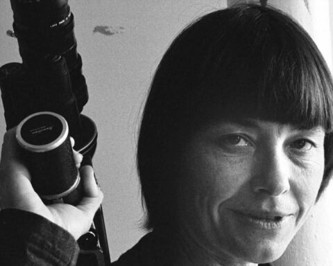 A black and white archival photo of a young Barbara Hammer. She is holding a camera and seen in close-up.