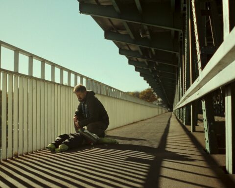 A man bends down beside the railing of a bridge, examining a dummy shaped like a human body.