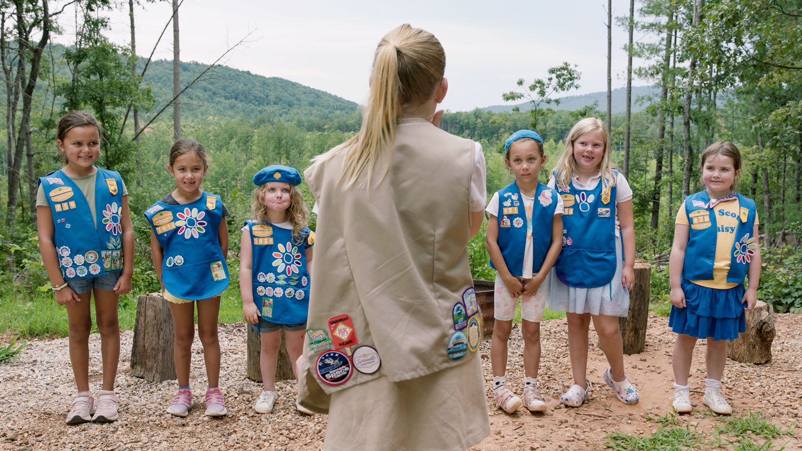 Five Girl Scouts in uniform face their leader, who has her back to the camera.