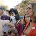 Congresswoman Sarah McBride speaks to reporters outside a voting station. She is wearing a read suit.
