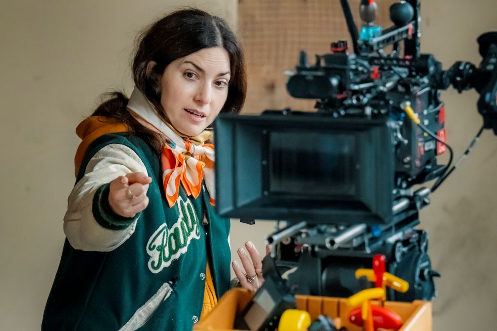 Filmmaker Rebecca Zlotowski directs on a film set. She is wearing a baseball jacket and standing in front of a camera.