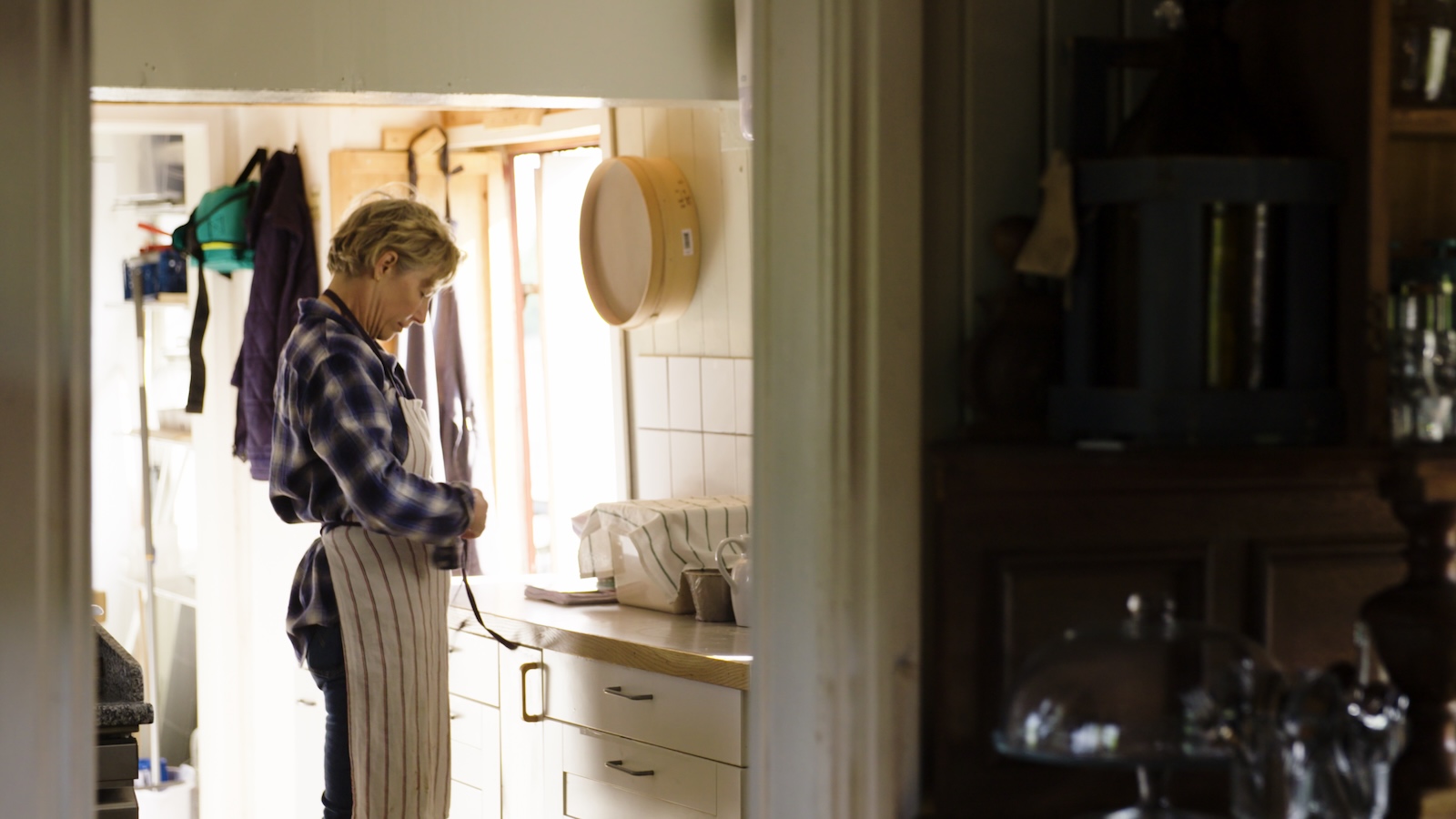 Pastry Chef Meg Ray stands in a kitchen, facing a counter. The scene is lit with natural light.