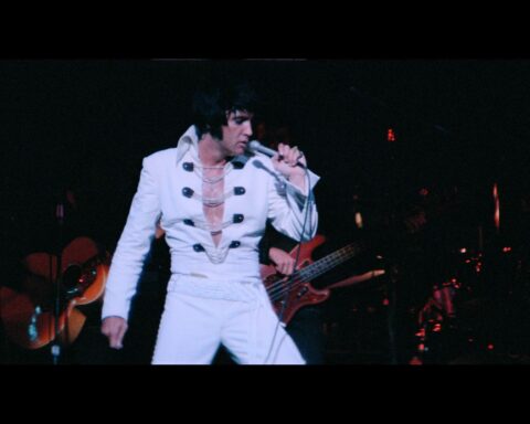 Elvis Presley performs in concert wearing a whte jumpsuit.