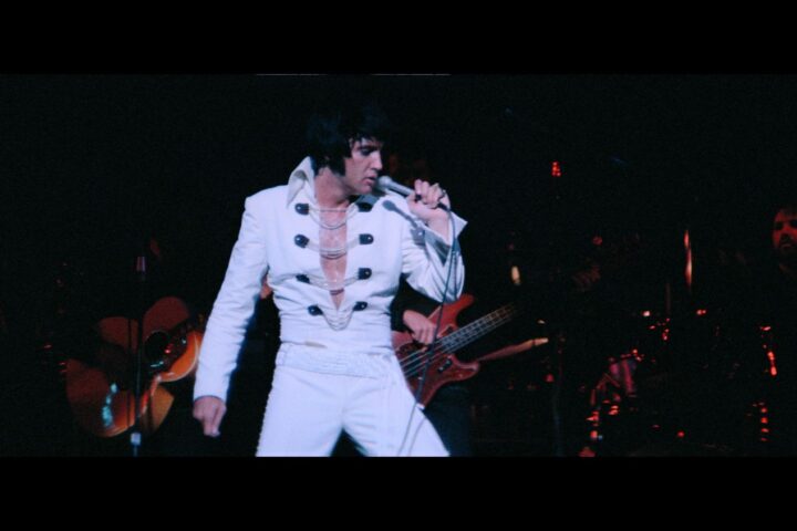 Elvis Presley performs in concert wearing a whte jumpsuit.